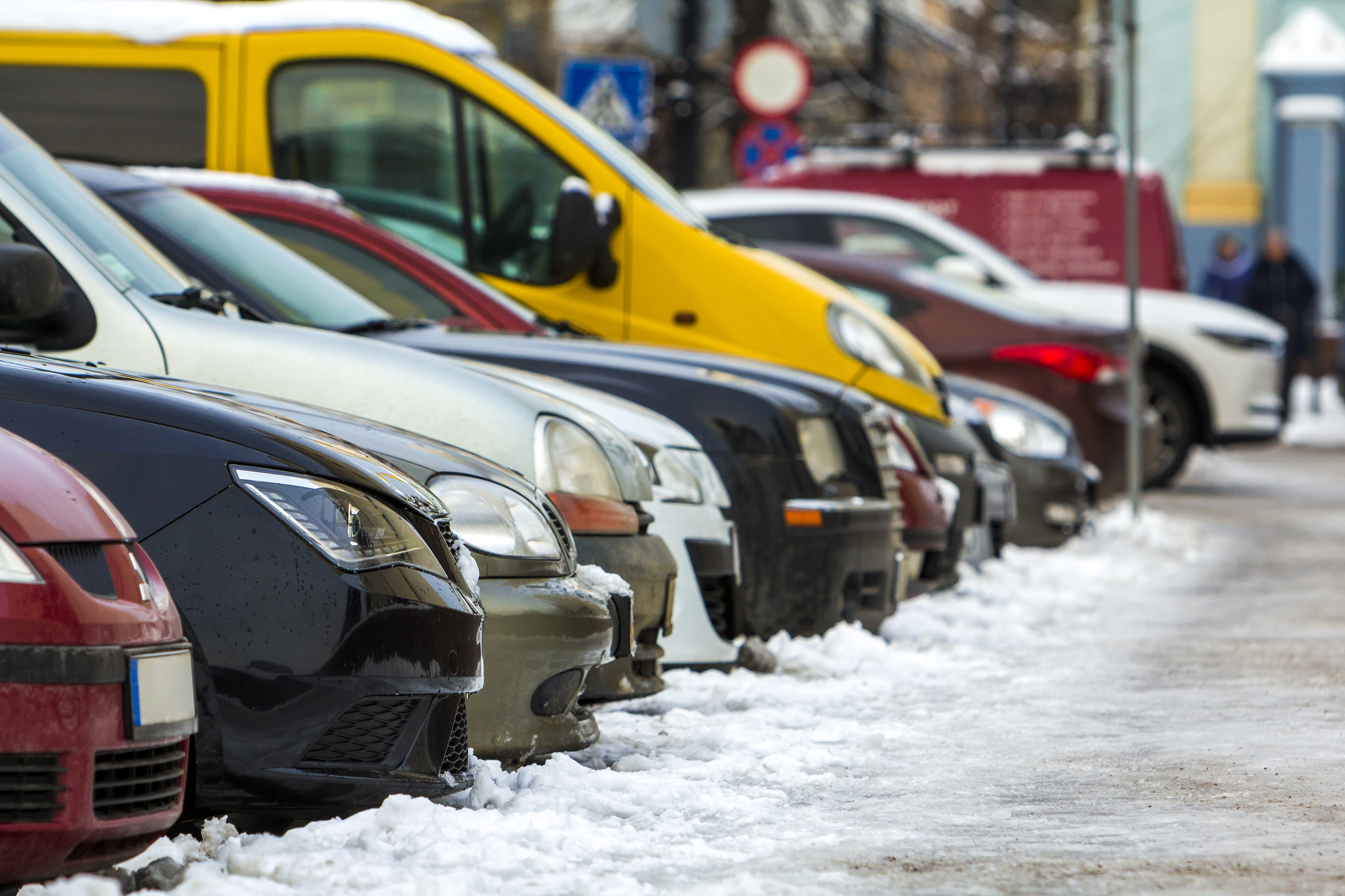 row of different types of cars parked along a snowy curb